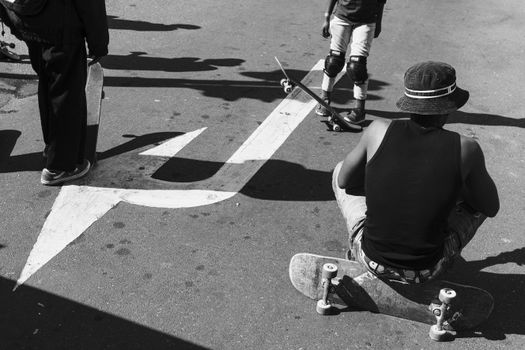 Black and white image of skateboarders resting on a road with bold arrow markings, creating a vibrant street culture vibe.