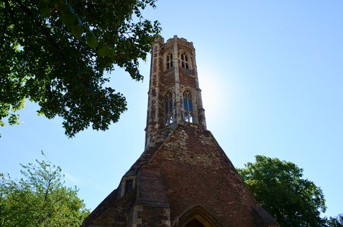 Free A historic brick tower rises against a clear blue sky, surrounded by lush green trees. Stock Photo
