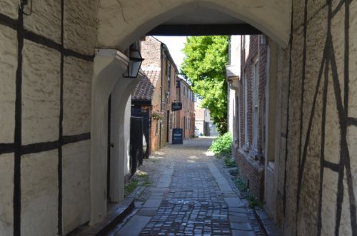 Free Scenic view of a cobblestone alleyway through an arched entrance with historic architecture. Stock Photo