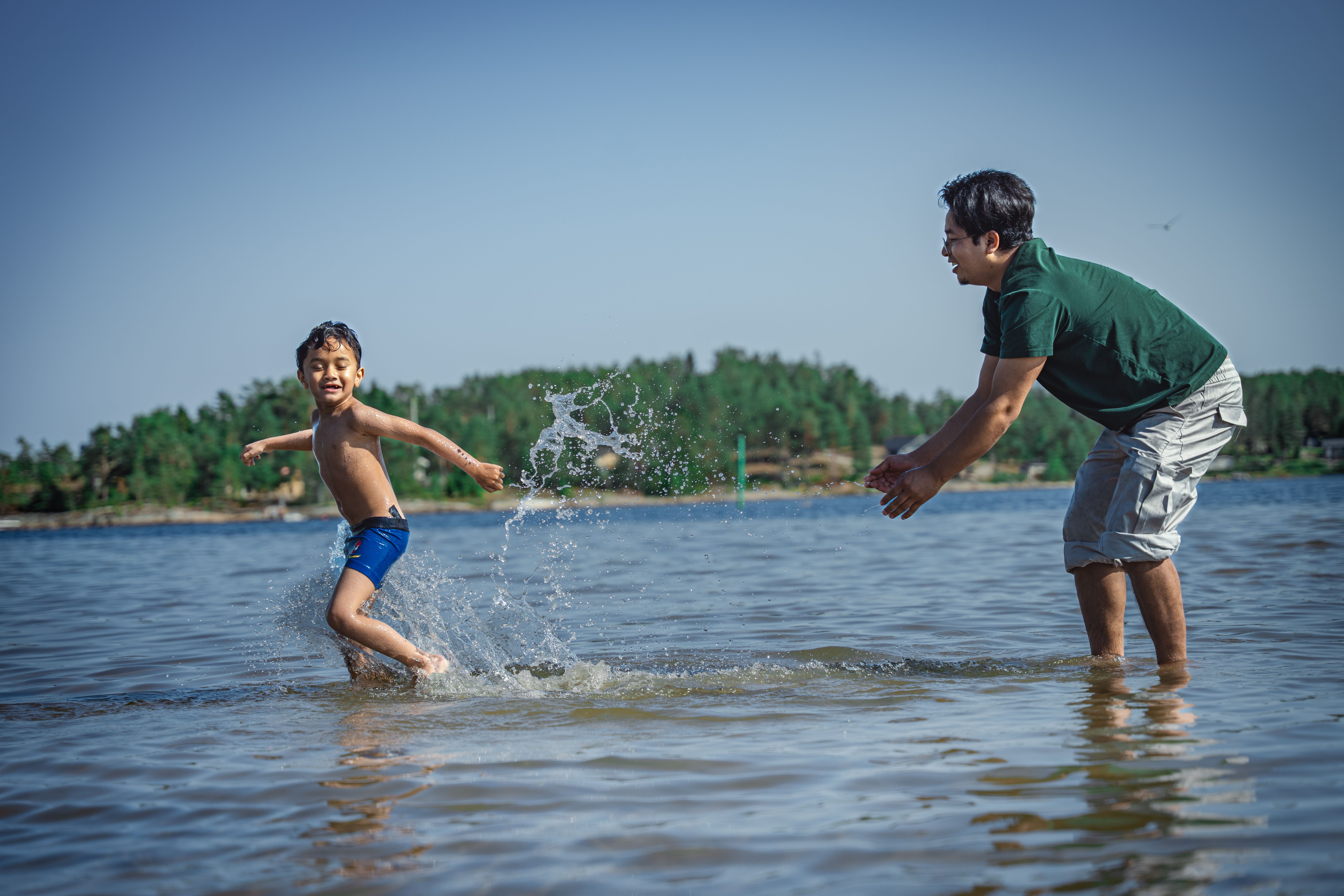 A father and son playing in shallow water at the beach, enjoying a sunny summer day.