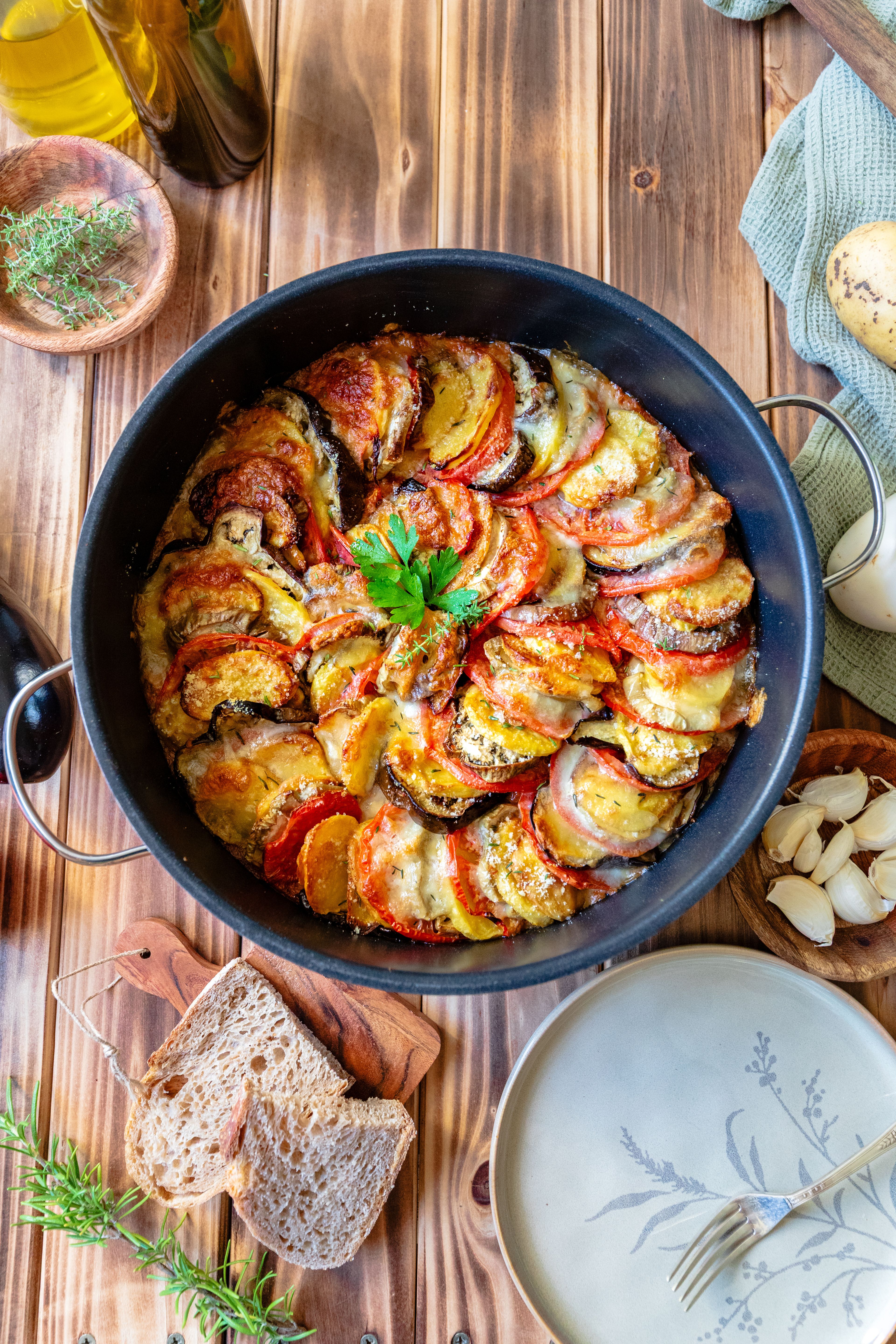 Golden ratatouille with vegetables arranged in a spiral, with bread, garlic and herbs on a wooden table