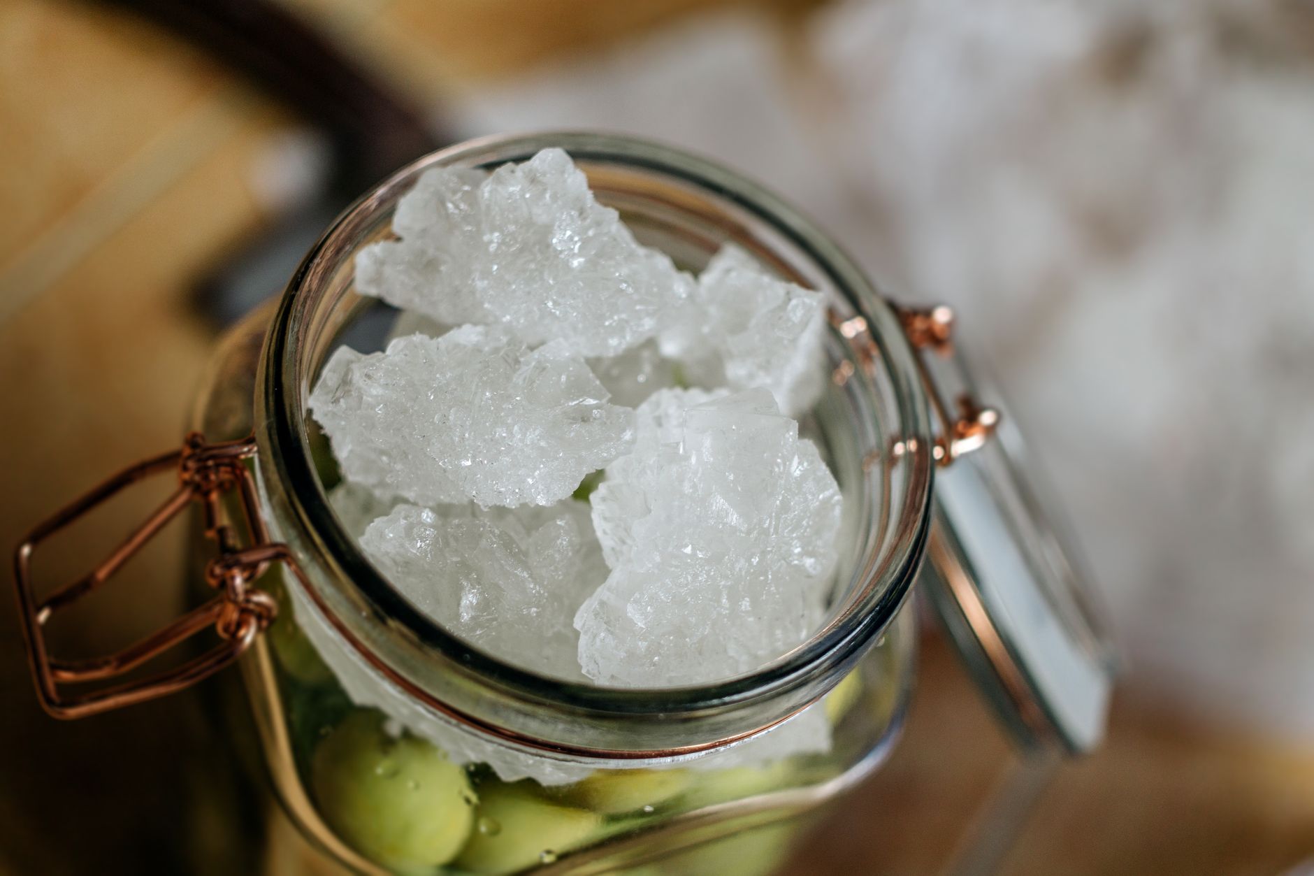 From above of glass jar with fresh green olives with cold ice placed on table