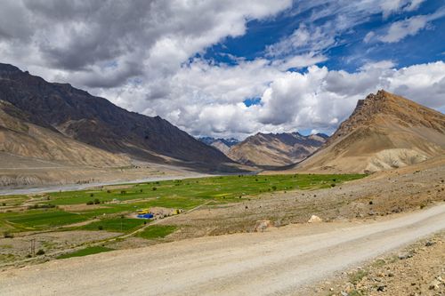 Free Expansive view of a green valley surrounded by towering Himalayan mountains under a vibrant blue sky. Stock Photo