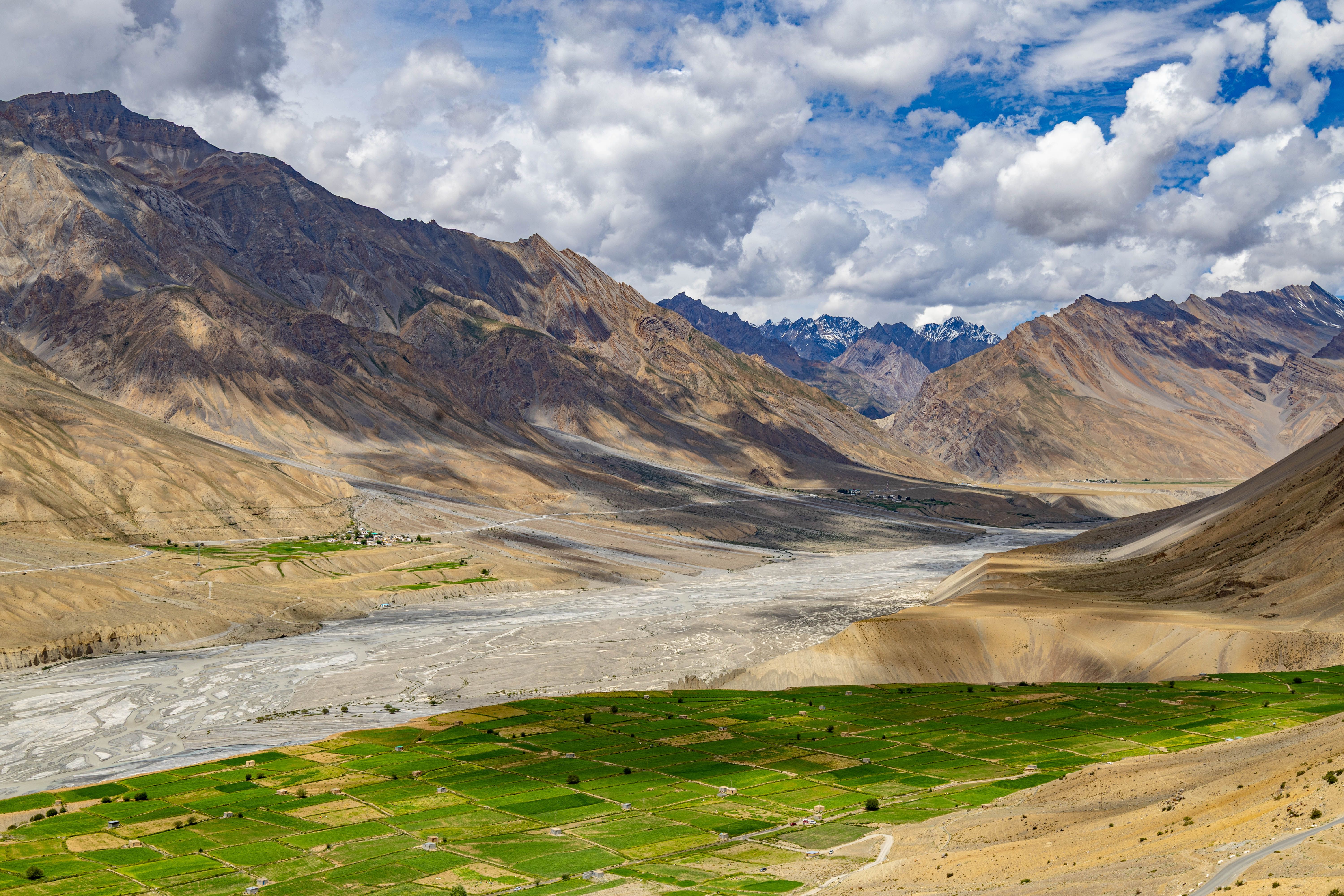Breathtaking view of a Himalayan valley with lush green fields and majestic mountains under a bright blue sky.