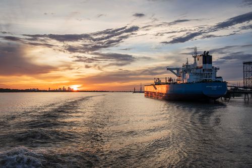 Free Beautiful sunset over a harbor with a cargo ship and city skyline in the distance. Stock Photo