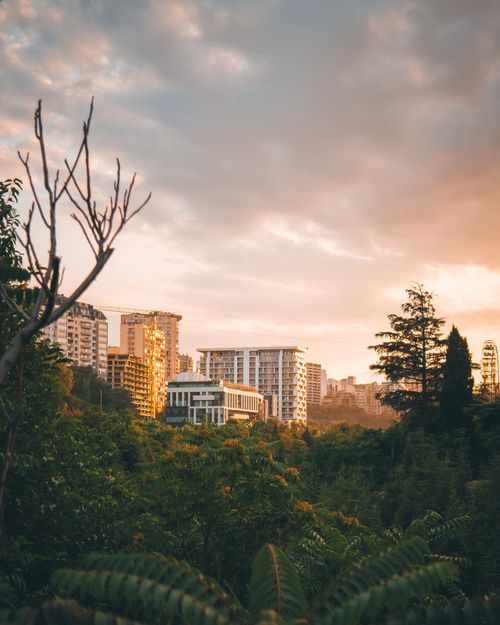 Free Stunning view of Tbilisi's skyline at sunset with modern buildings emerging above lush greenery. Stock Photo
