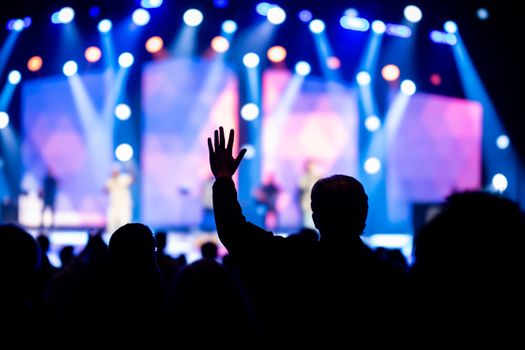Silhouette of an audience member reaching out towards a brightly lit concert stage.
