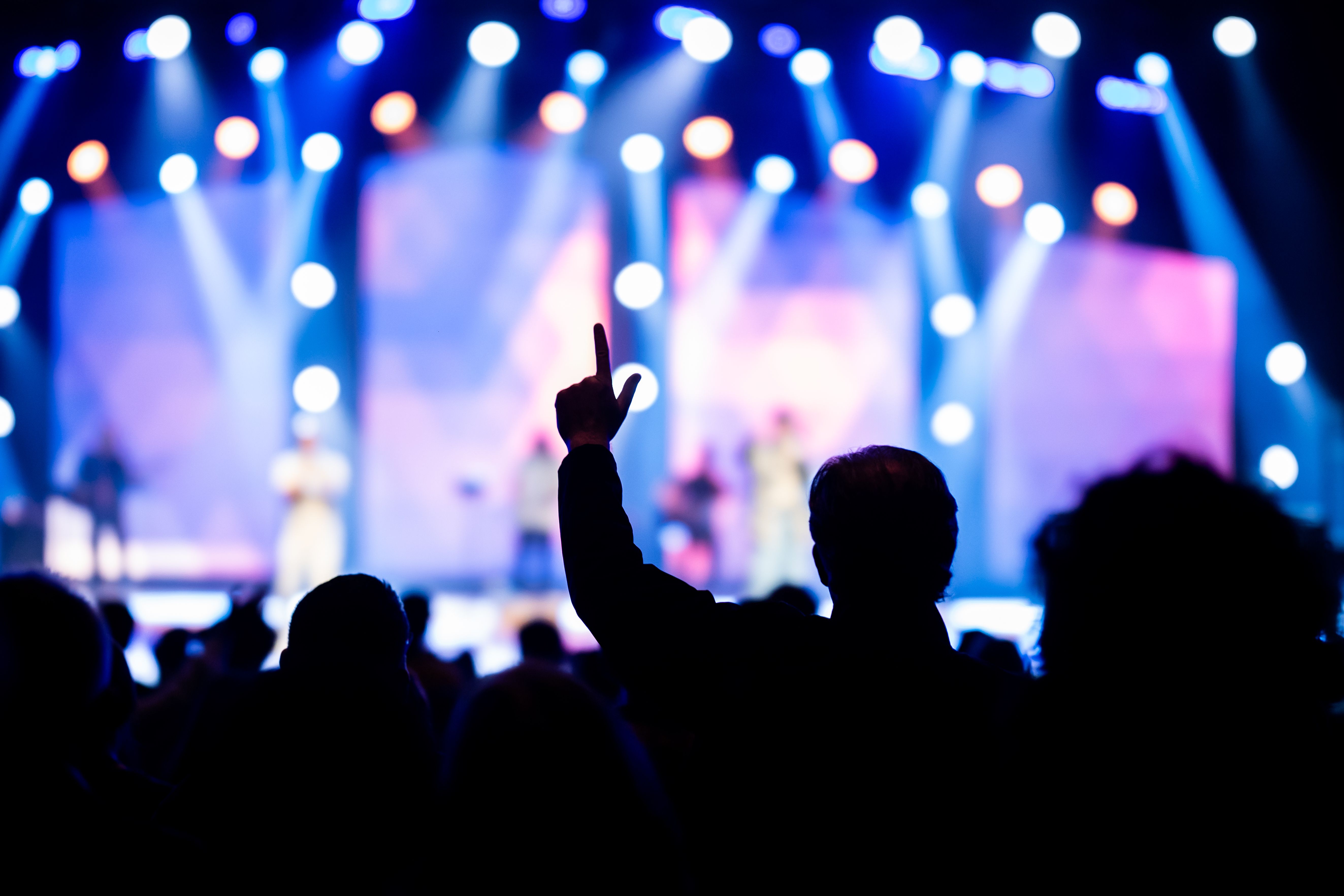A backlit concert crowd raises a hand toward stage lights during a live show