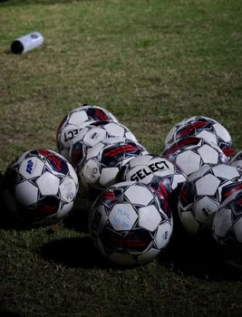 A group of soccer balls on a grassy field, indicating a nighttime training session in Singapore.