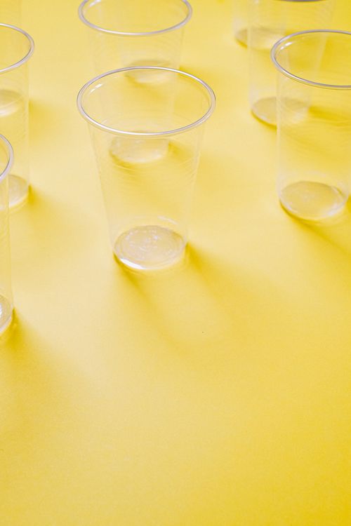 Free Clear plastic cups arranged on a vibrant yellow background, casting shadows. Stock Photo