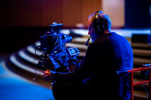 Free Cameraman operating a video camera with headset in a dimly lit environment. Stock Photo