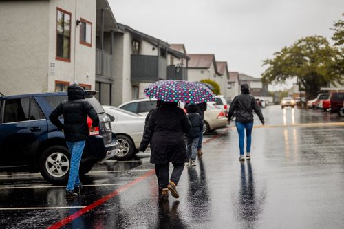 Free People walking on a wet street under a colorful umbrella during a rainy day. Stock Photo