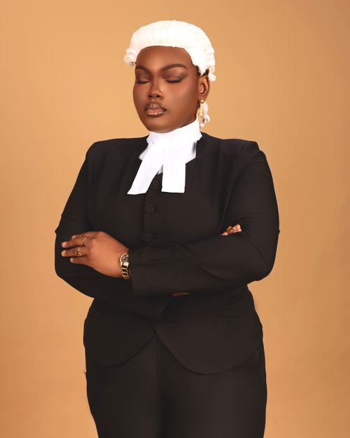 Free Confident female lawyer in formal attire with wig, posing against a neutral background. Stock Photo