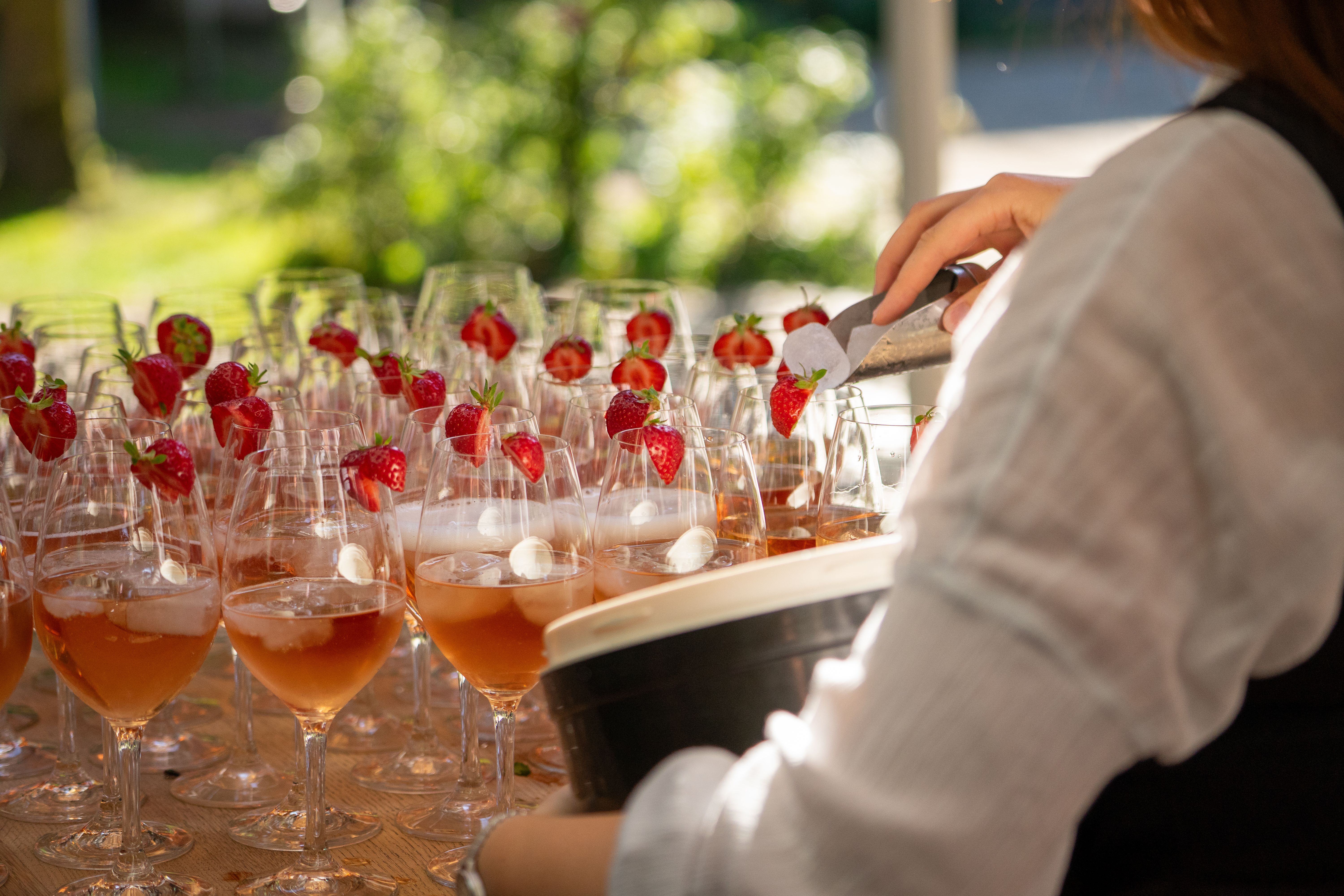 Close-up of a bartender adding ice to strawberry cocktails at an outdoor gathering.