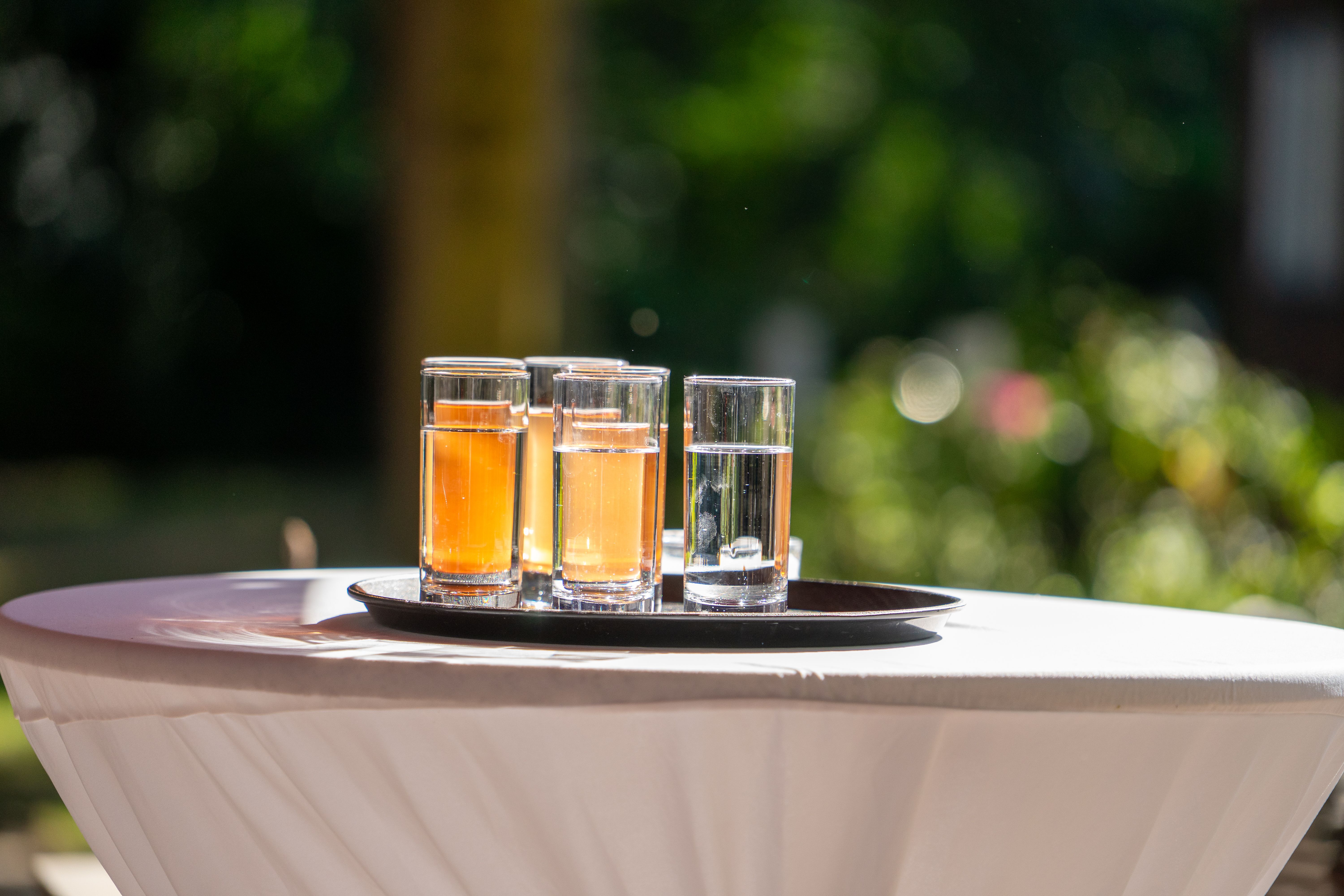 Three glasses with beverages on a tray, placed on a table outdoors under sunlight. Ideal for summer themes.