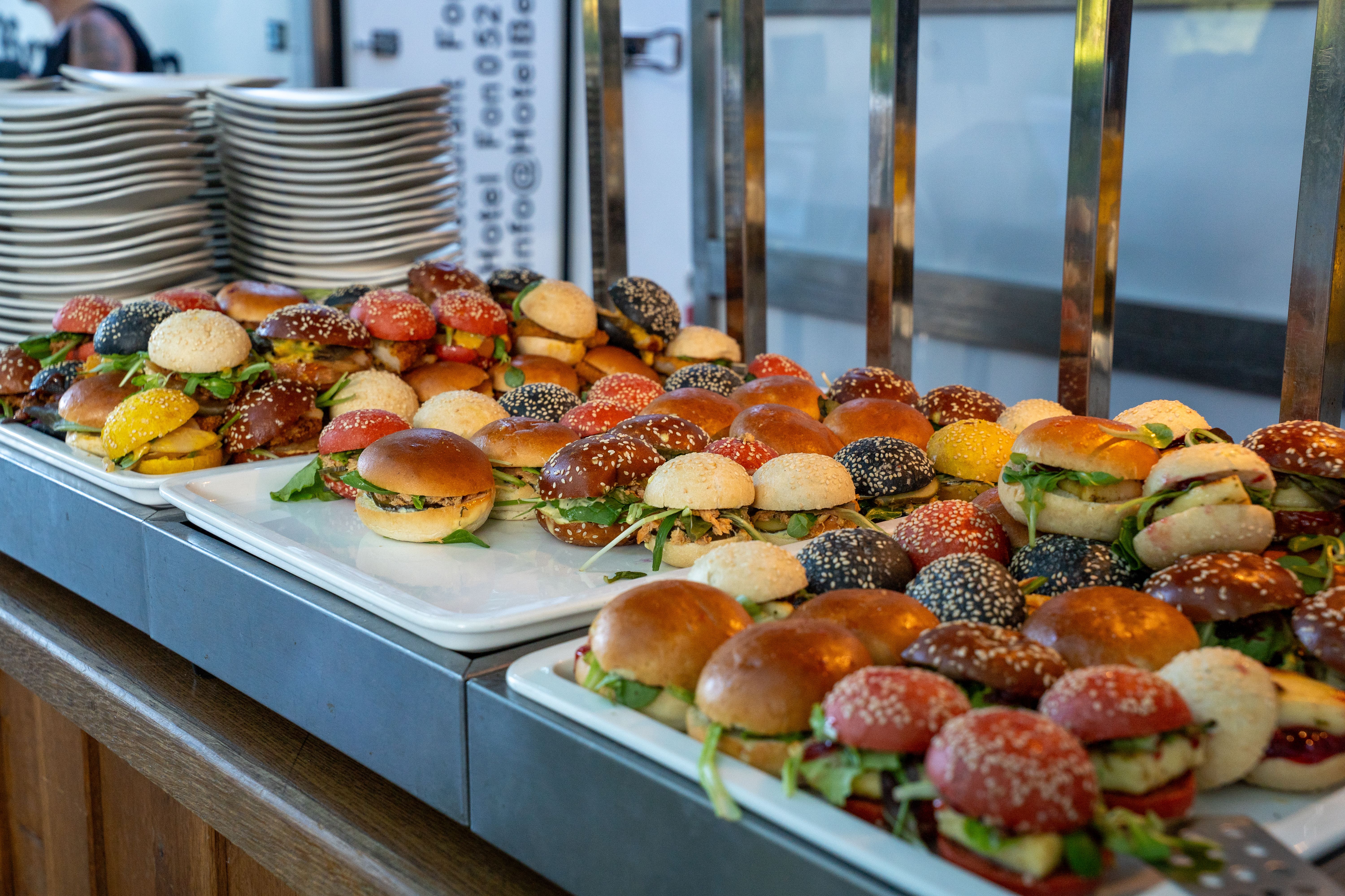 A variety of colorful mini burgers displayed on trays at a buffet.