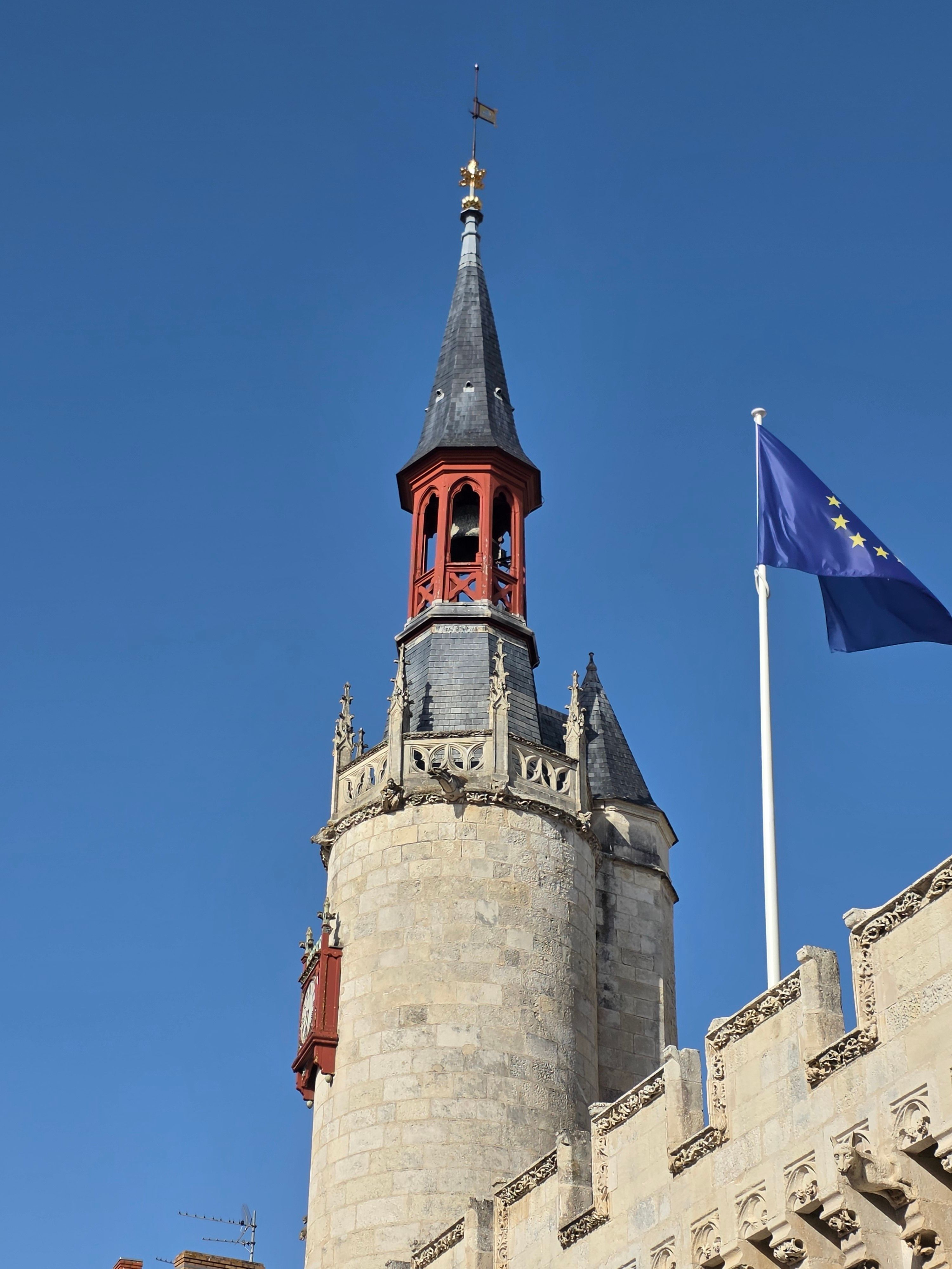 Photograph of a historic tower and EU flag under a clear blue sky in La Rochelle, France.