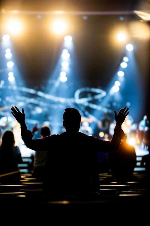 Free Silhouette of a person worshipping at a lively concert indoors with bright stage lights. Stock Photo