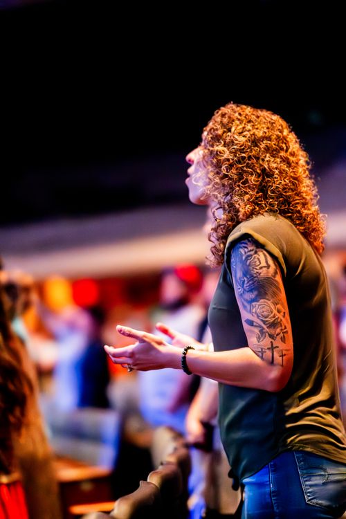 Free Curly-haired woman with tattoos worshiping at a lively indoor event. Stock Photo