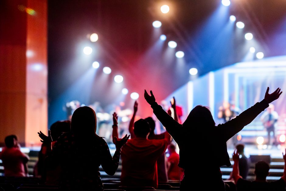 Fotomural Un público entusiasta, con las manos en alto, disfruta de un concierto en directo con una colorida iluminación en el escenario.