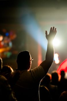 A person raises their hand in a vibrant concert atmosphere.