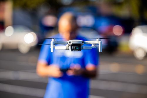 Free Close-up of a drone hovering with a blurred man operating in the background outdoors. Stock Photo
