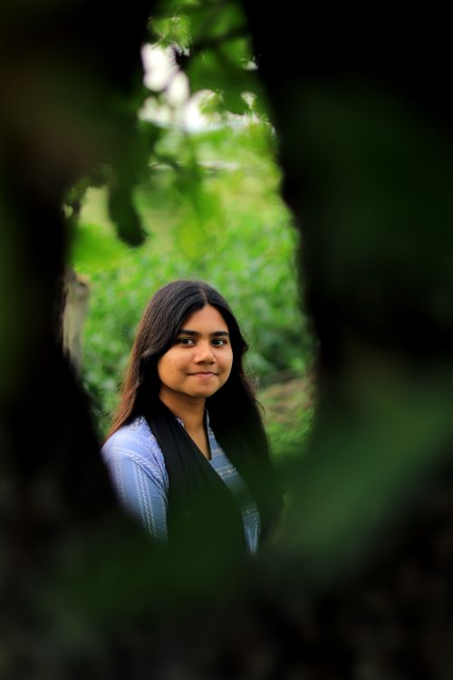 Free A young woman smiling, surrounded by lush green leaves and branches. Stock Photo