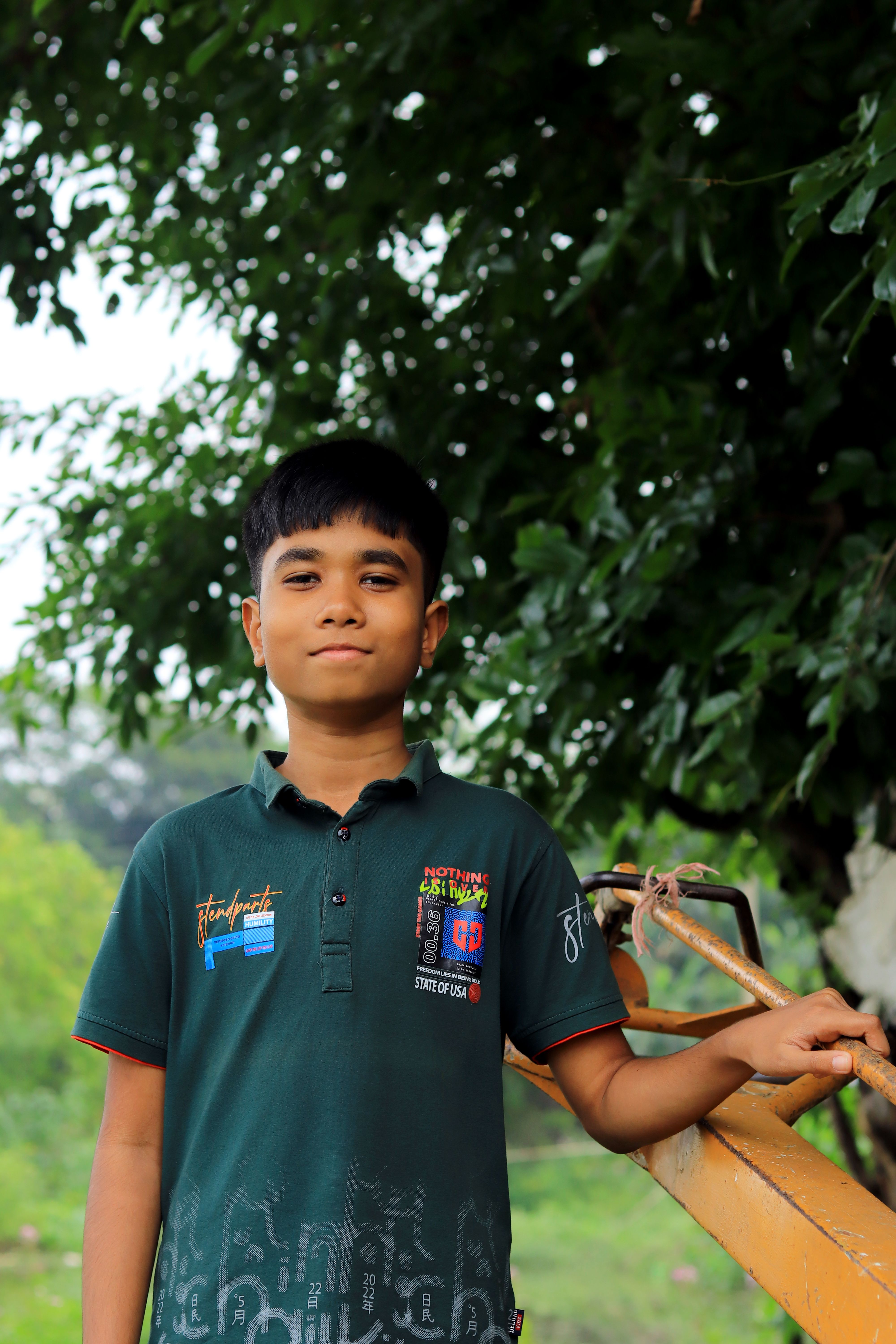 Portrait of a young boy outdoors, holding a stick, with lush green foliage in the background.