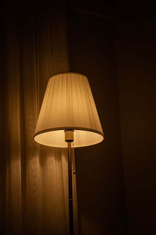 Free A warmly lit standing lamp casts a serene glow in a cozy indoor setting, perfect for a relaxing ambiance. Stock Photo