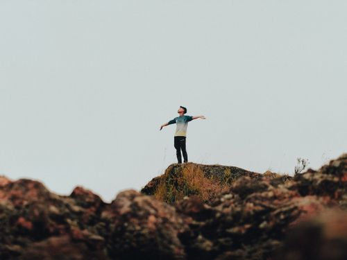Free A man standing on a rocky outcrop with arms outstretched, embracing freedom in a natural setting. Stock Photo