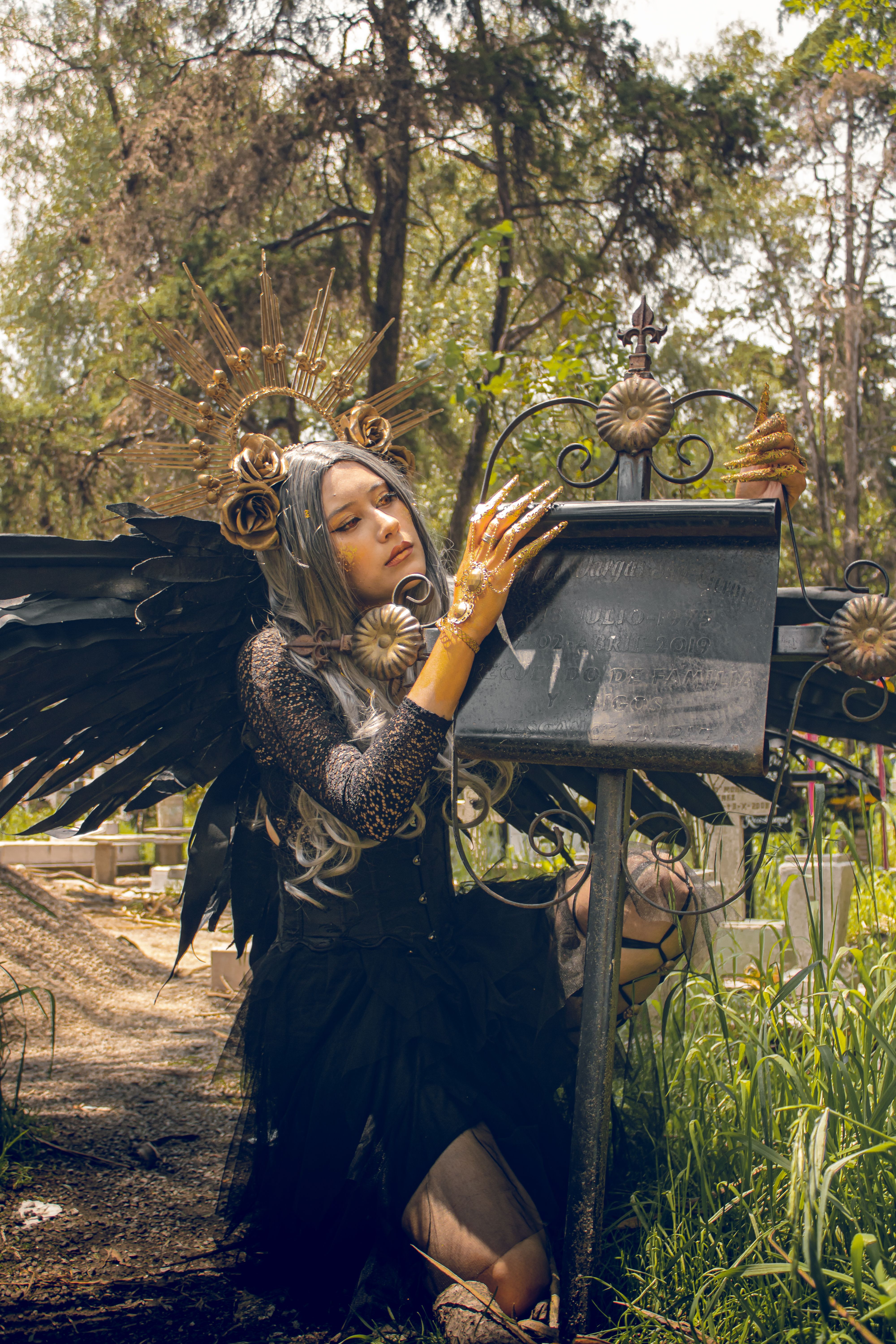 A cosplayer in gothic makeup and wings poses in a cemetery, capturing a mystical scene.