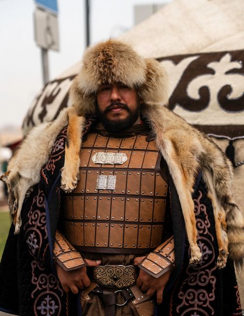Free Portrait of a Kyrgyz warrior in traditional attire with a yurt in the background. Stock Photo