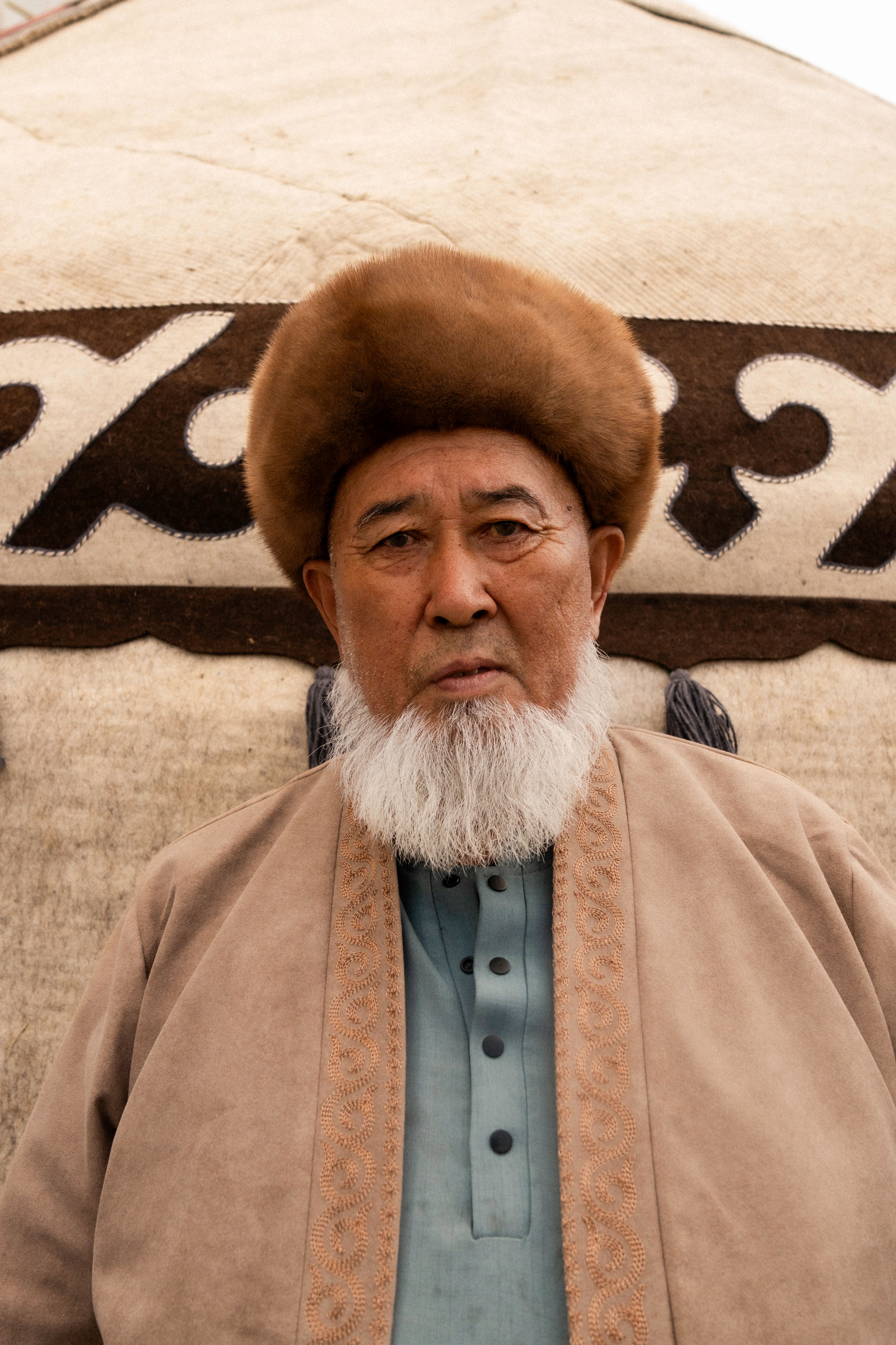 Elderly Kyrgyz man wearing traditional clothing in front of a yurt in Kyrgyzstan.