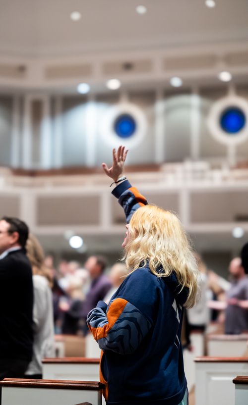 Free A woman with blonde hair raises her hand in a church service, expressing devotion. Stock Photo
