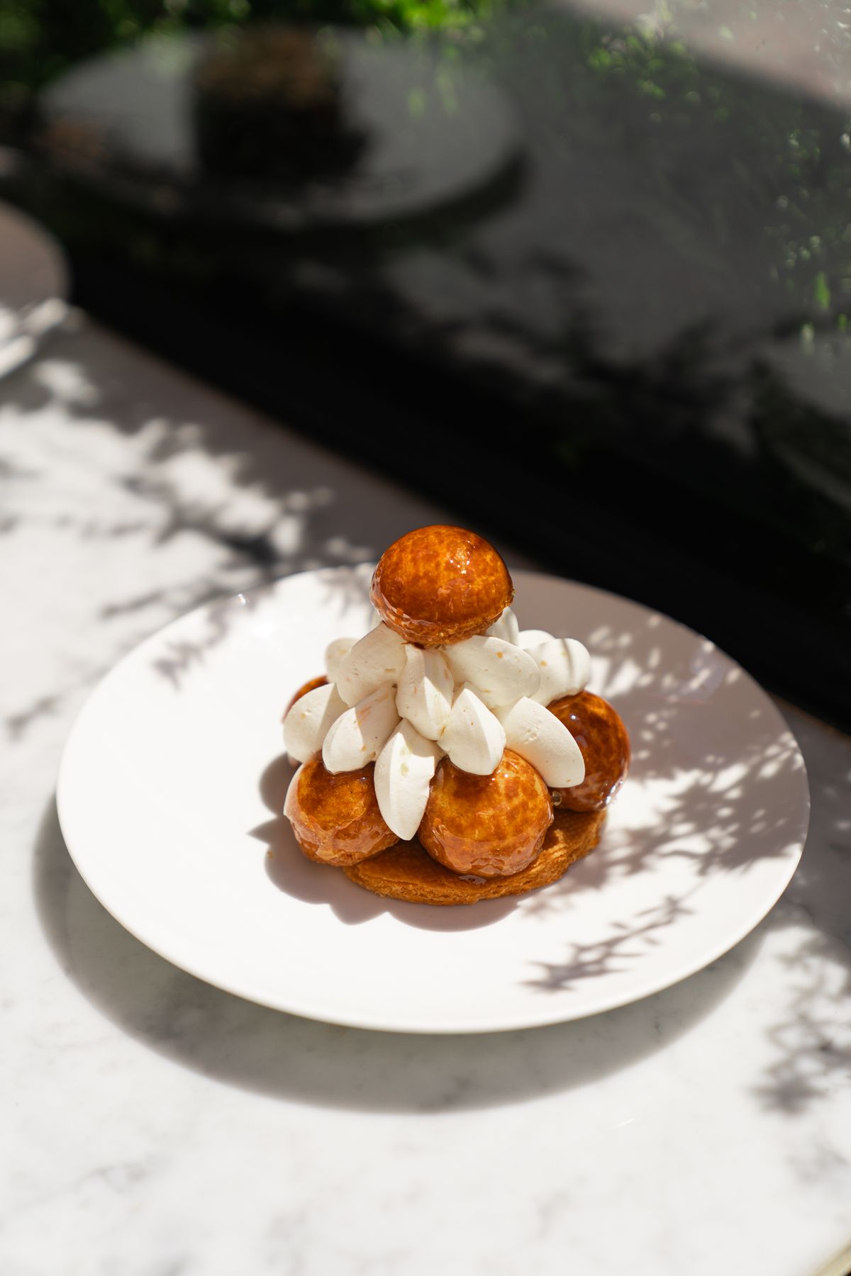 A Saint-Honoré on a white plate, caramelised choux around a piped centre.