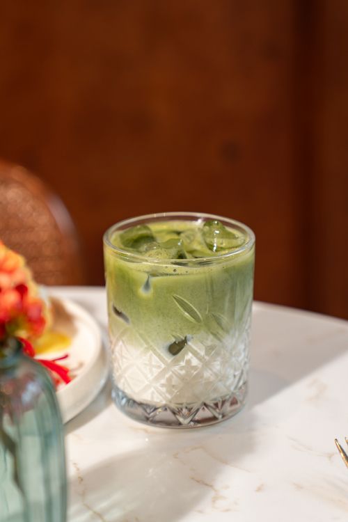 Free Chilled matcha latte in a decorative glass on a marble table with floral accents. Stock Photo