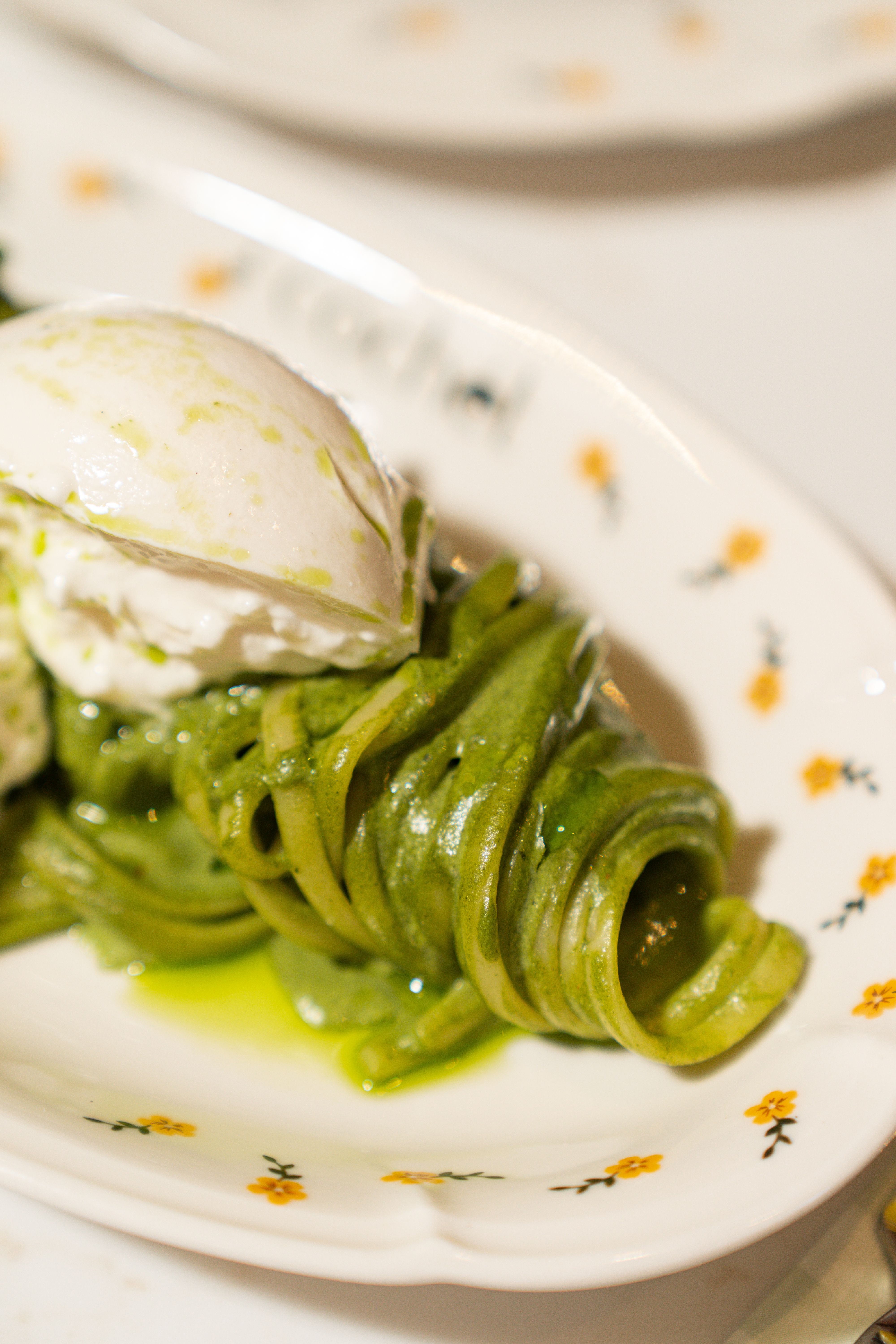 Delicious spiral green pesto pasta topped with creamy mozzarella on elegant dish.