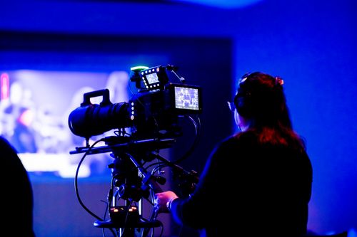 Free A cameraperson operates a professional camera in a low light studio setting, capturing footage. Stock Photo