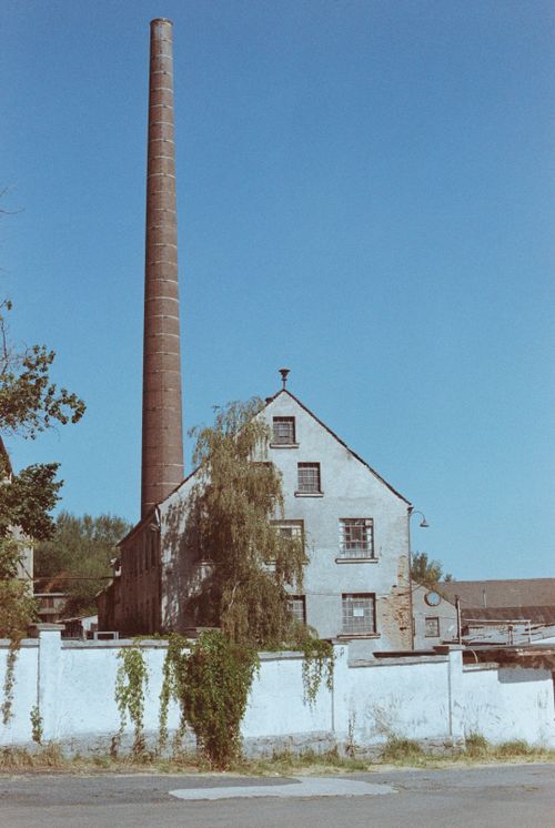 Free A vintage industrial building featuring a tall smokestack set against a clear blue sky. Stock Photo