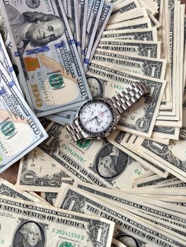 A luxury watch placed on a pile of various US dollar bills, symbolizing wealth and time management.