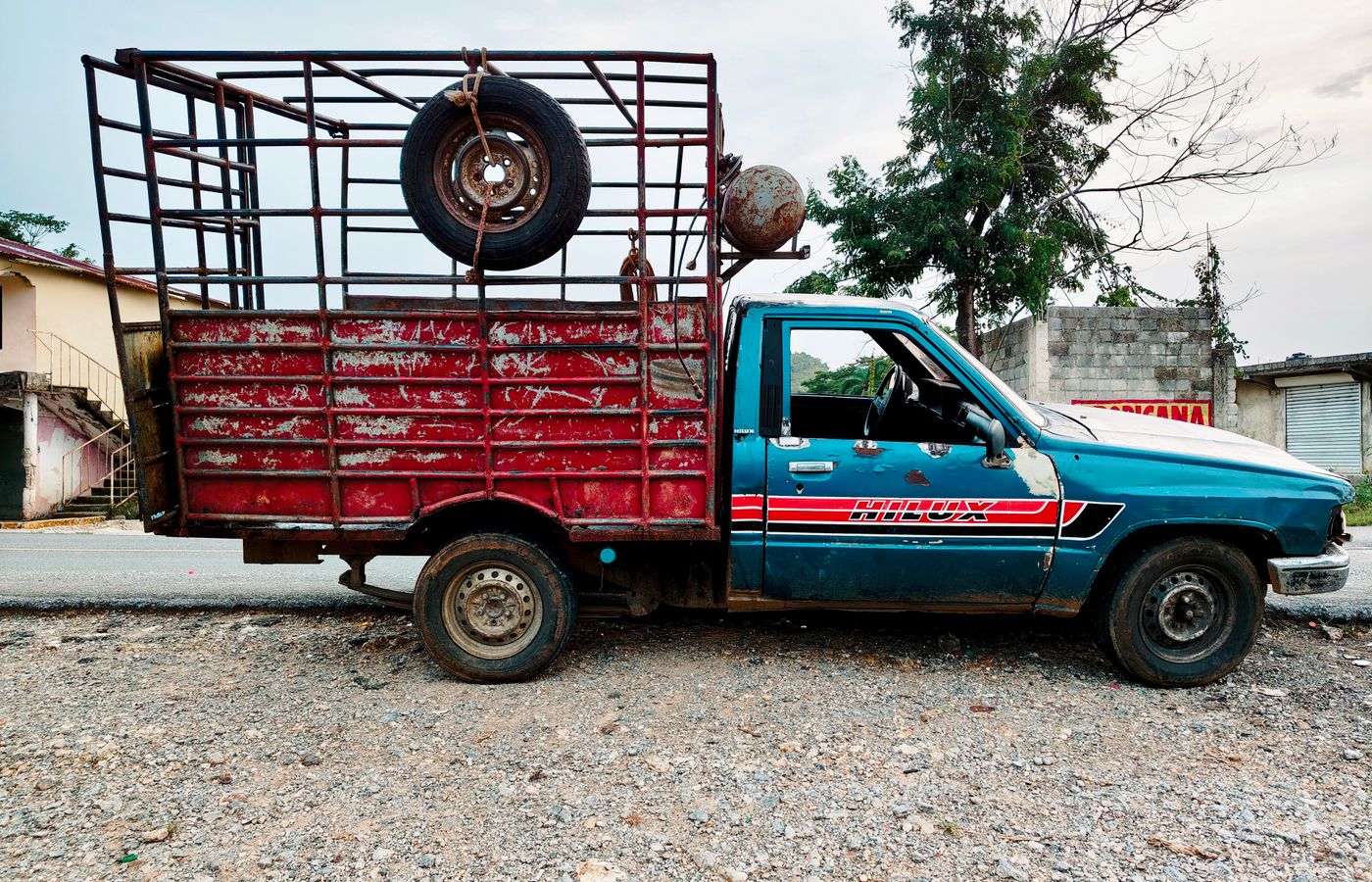 Old blue and red pickup truck with a metal cage parked on a gravel road.