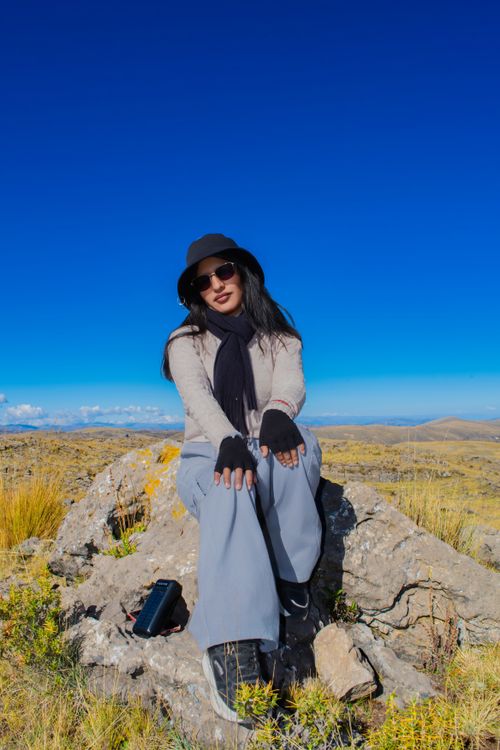 Free A woman in stylish attire enjoys a sunny day outdoors on a rocky hillside. Stock Photo