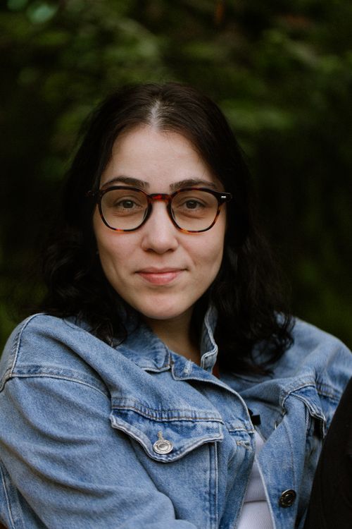 Free Portrait of a young woman with glasses in a denim jacket, smiling outdoors. Stock Photo