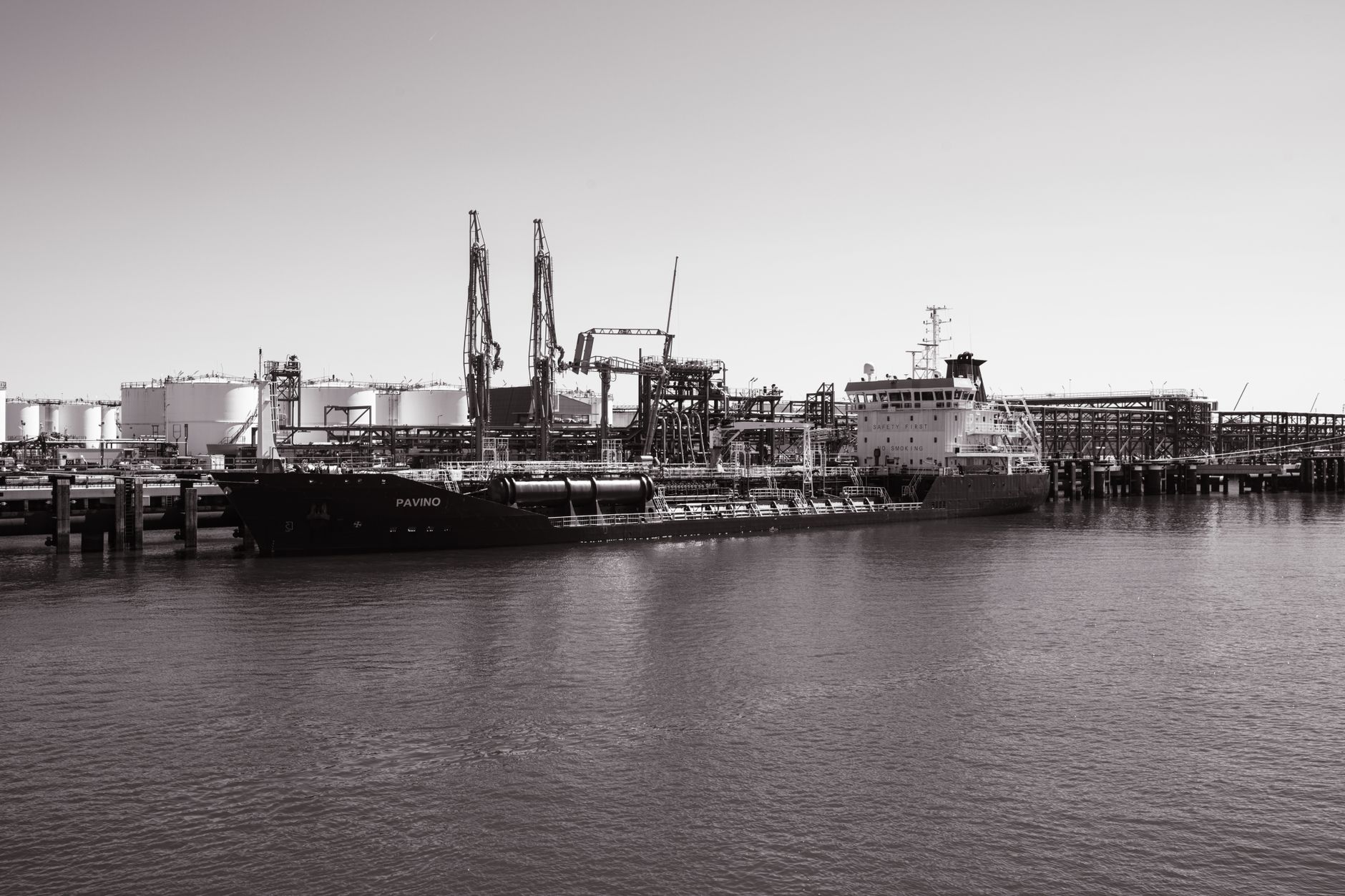 Illustrative photograph: Monochrome photo of a cargo ship docked at an industrial port with cranes in the background.