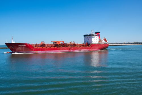 Free A vibrant red cargo ship navigates through calm ocean waters on a clear sunny day. Stock Photo