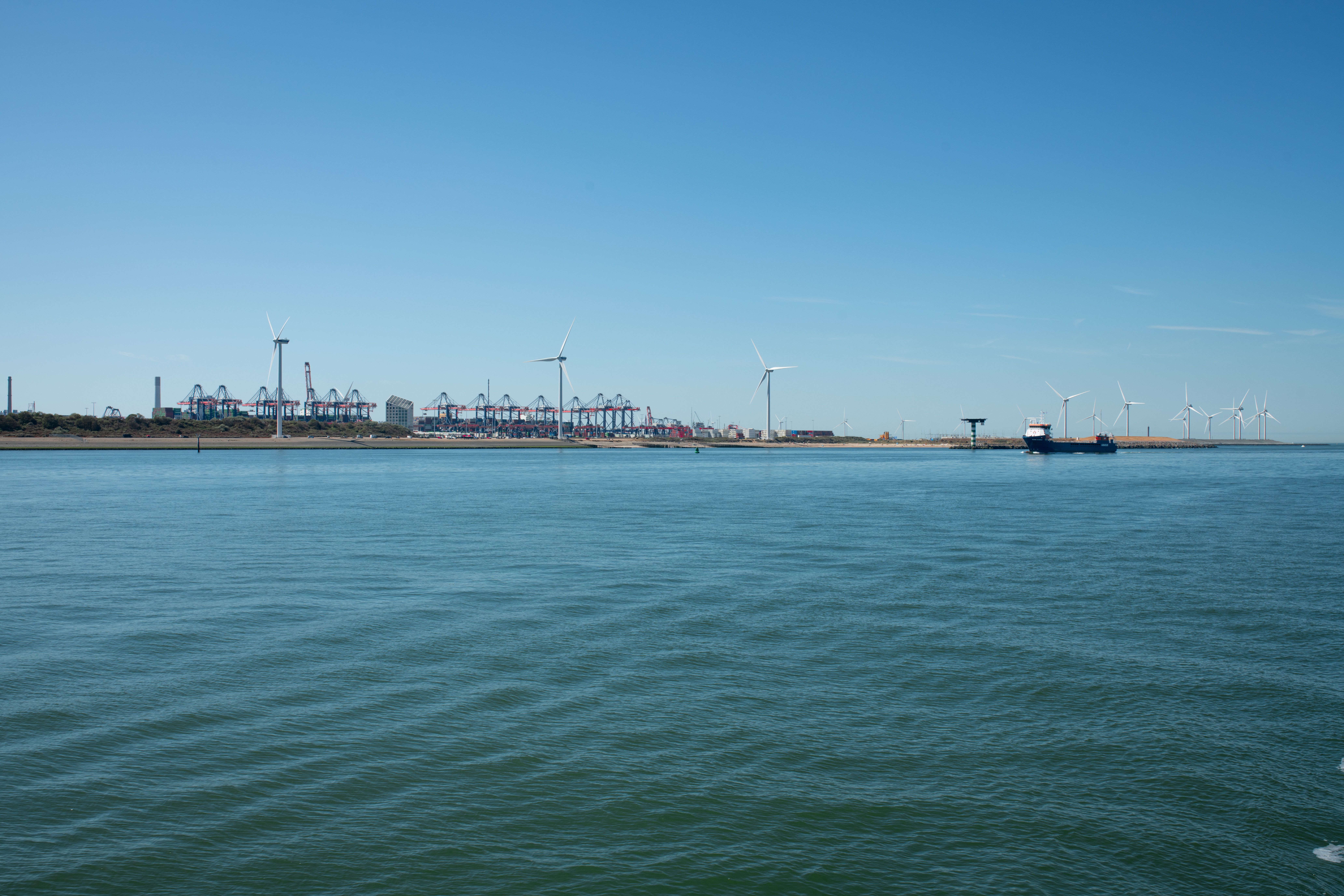 Illustrative photograph: A scenic view of a coastal wind farm near a shipping port, showcasing renewable energy and maritime activity.