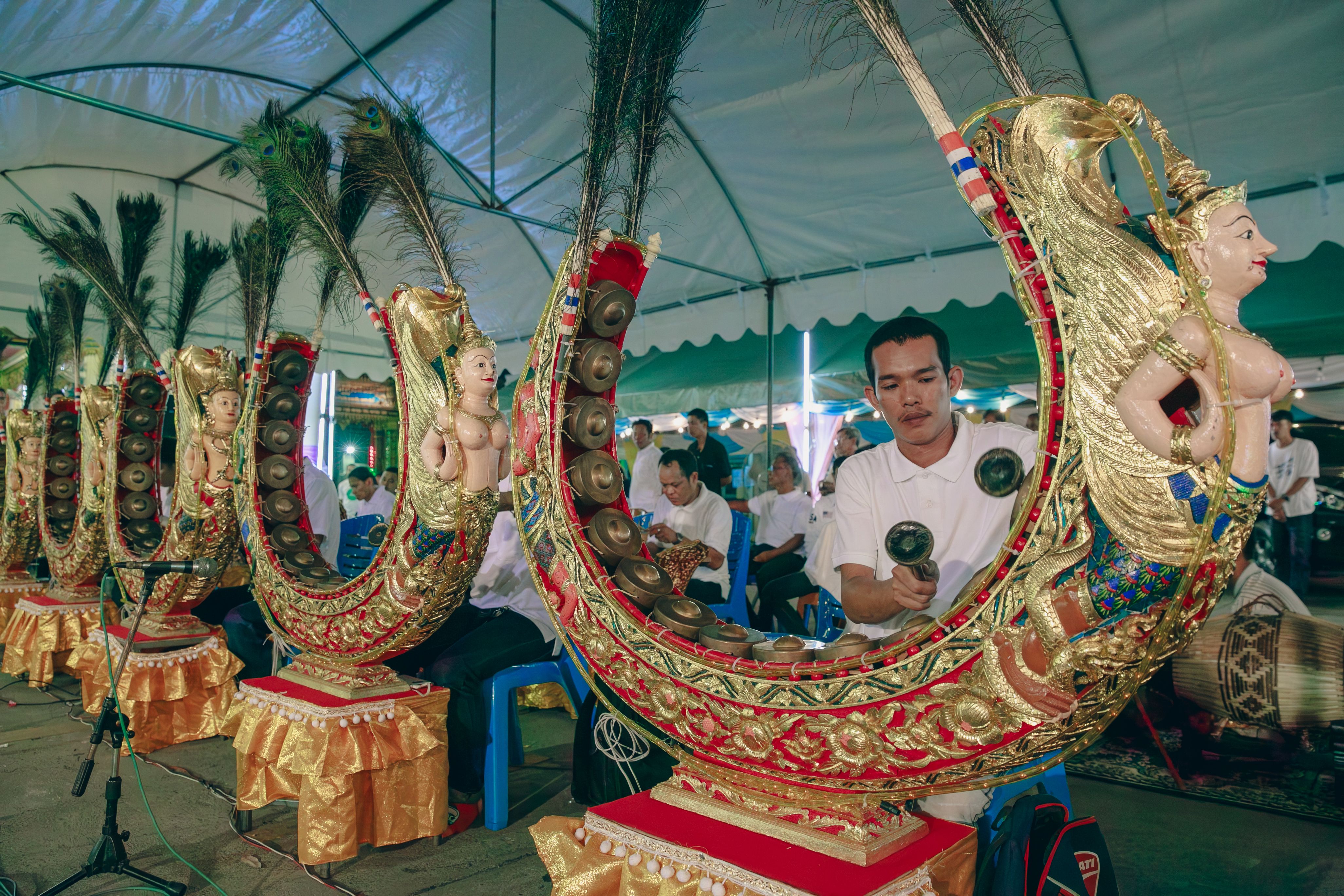 Musicians playing traditional Southeast Asian instruments in an indoor setting under a tent.