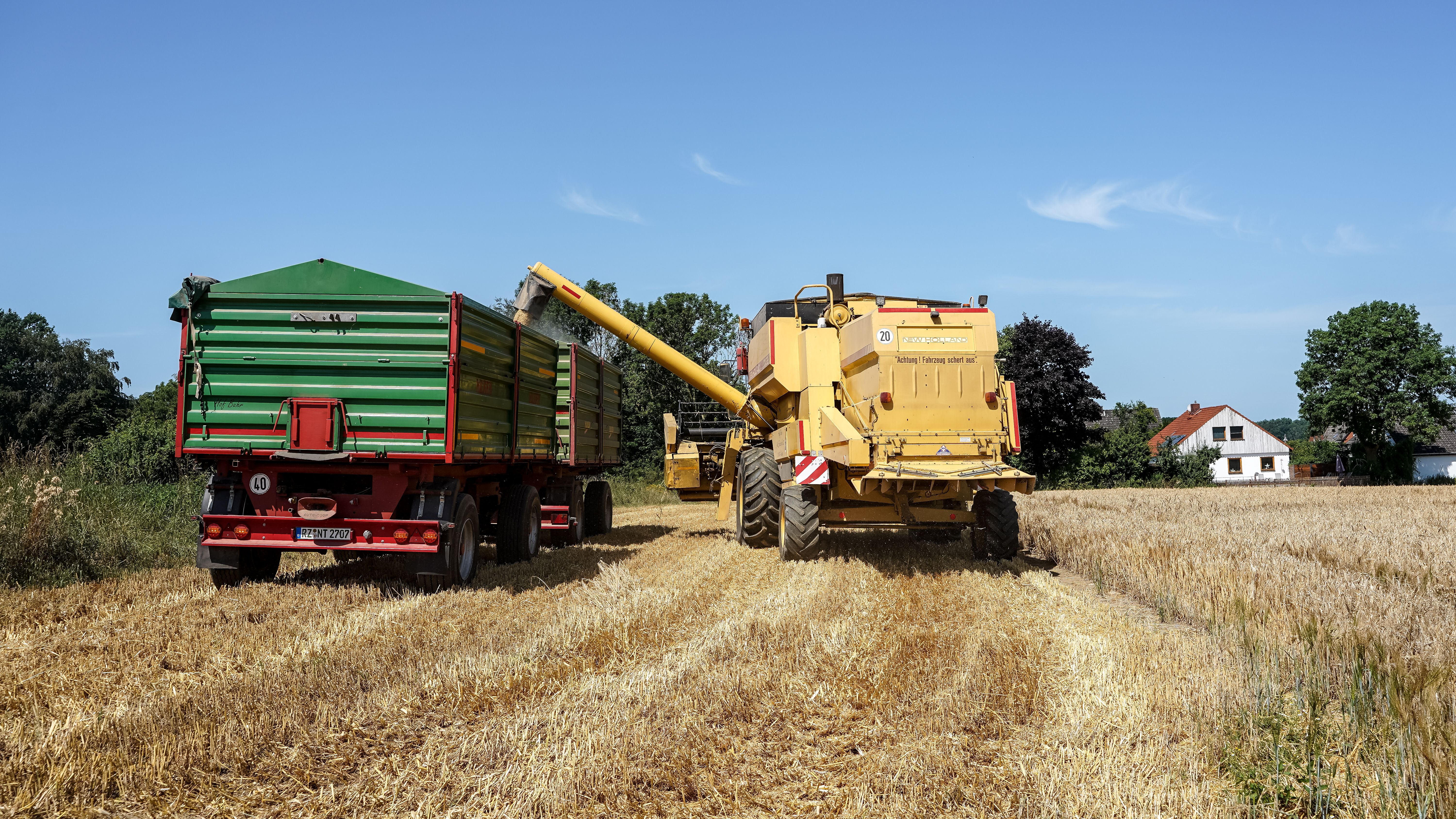 A combine harvester unloading into a trailer during summer harvest in Lütau, Germany.