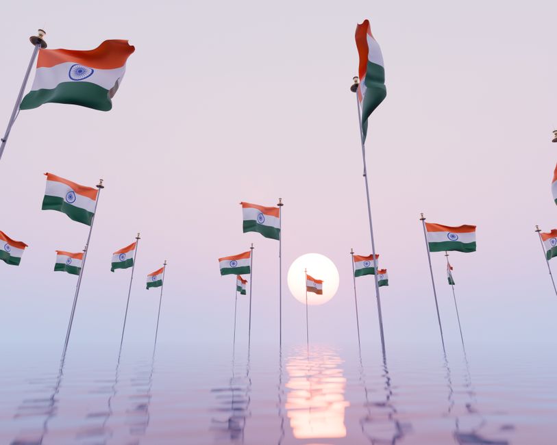 Multiple Indian flags waving with the sunrise over water, symbolizing patriotism and national pride.