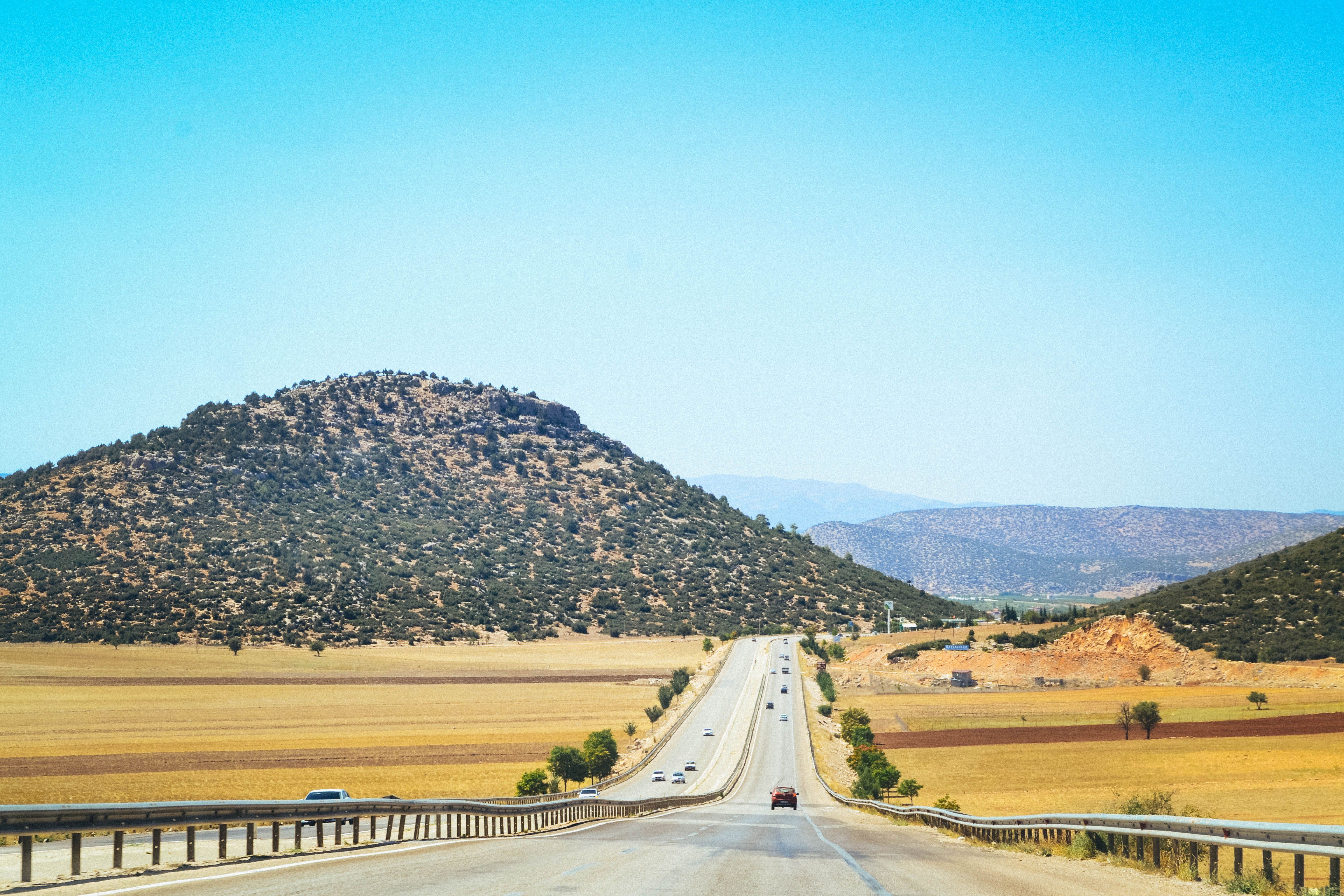 Long straight road through scenic hills under a bright clear sky, perfect for outdoor journeys. - Photo by Oğuzhan Çoban on Pexels